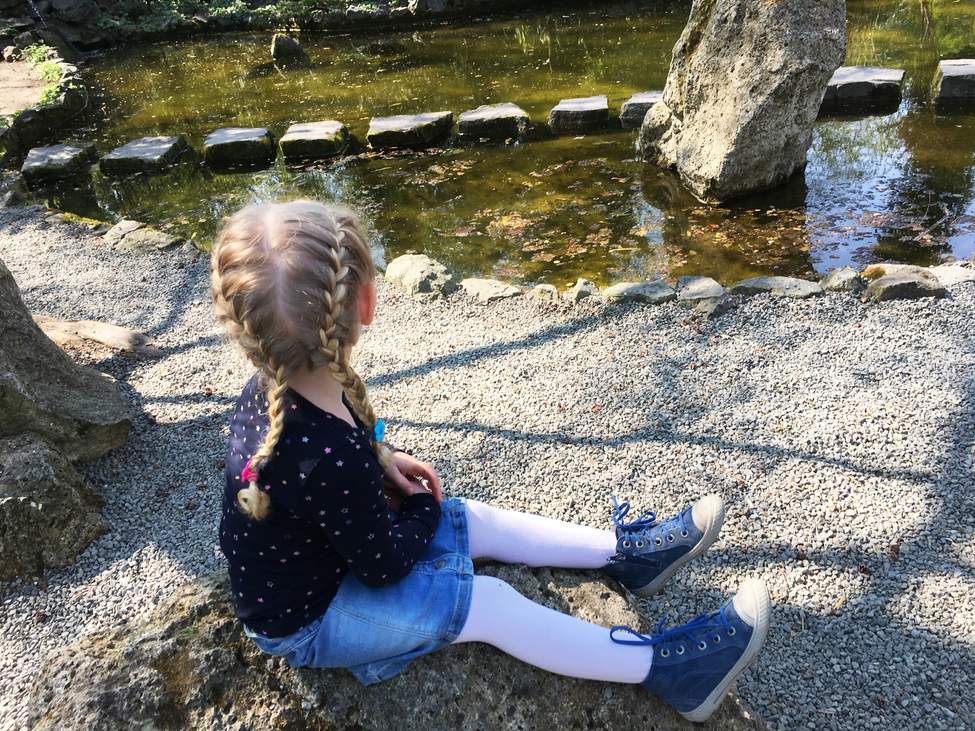 Kislány ül egy kis tó partján a Füvészkertben