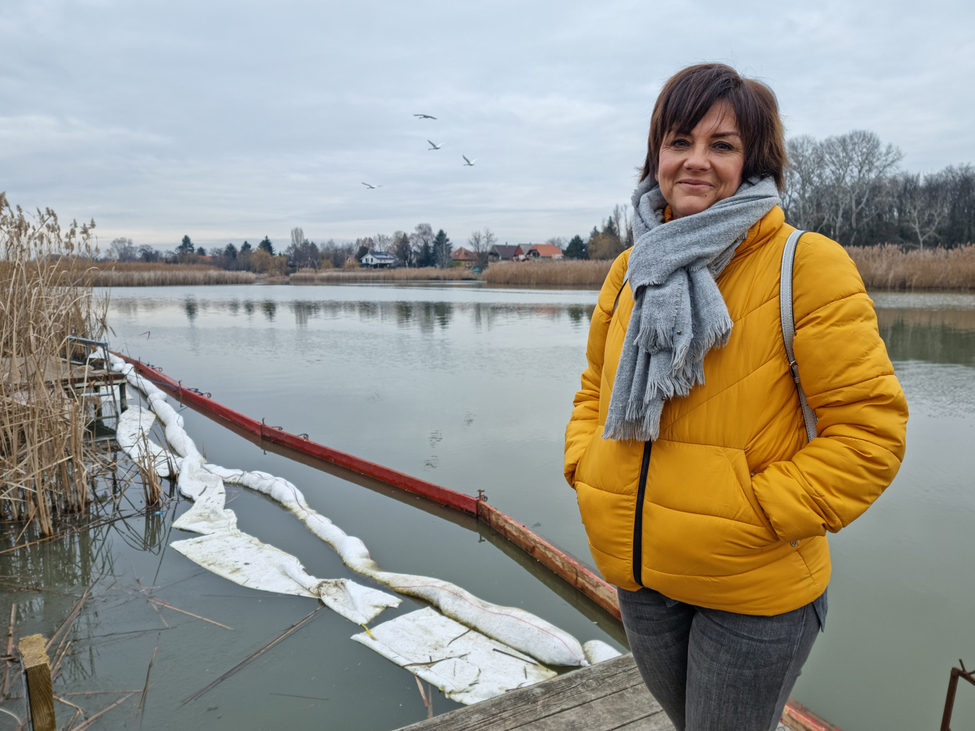 Siklós Gabriella, az Országos Vízügyi Főigazgatóság szívivője a Duna-ágnál, amelyet sikerült a szennyezéstől megóvni. A vízen az úgynevezett szanul hurka látható, amely felszívja a maradék olajat is, illetve a mérések idejére állandósított fa védőfal